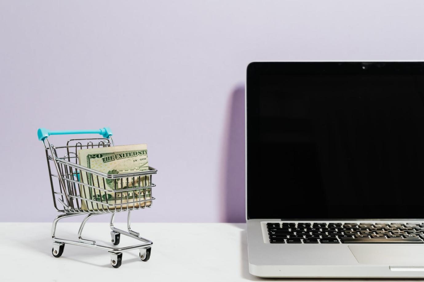 small shopping cart with money next to a laptop